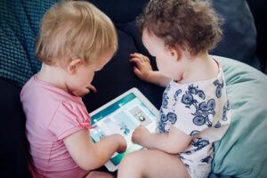2 toddlers playing tablet on the sofa