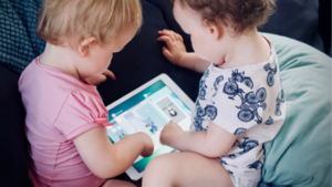 2 toddlers playing tablet on sofa