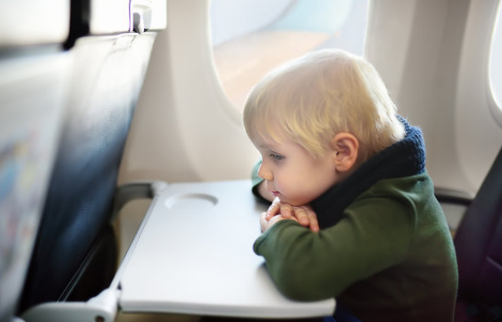 A toddler boy sitting by aircraft window during the flight
