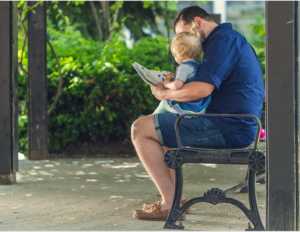 Man reading book to toddler on the bench